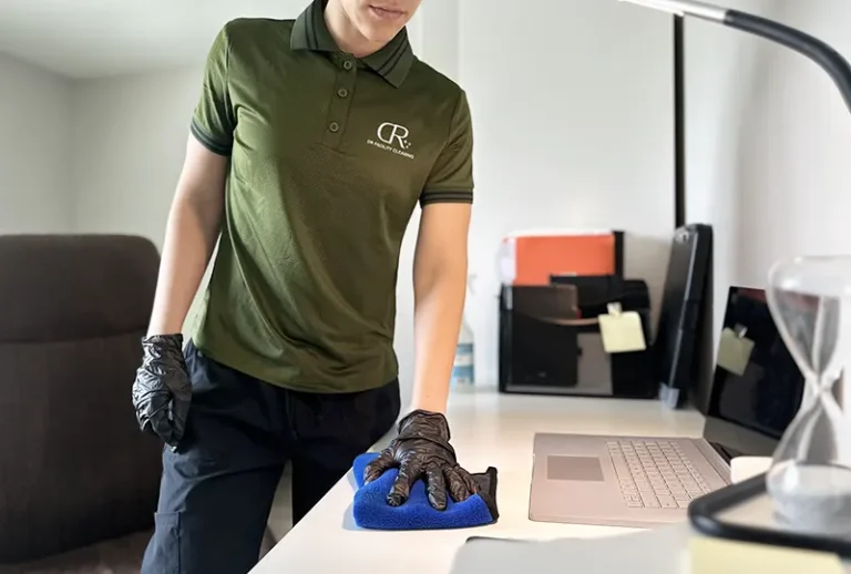 Professional cleaner wearing gloves wiping an office desk with a microfiber cloth in a modern workplace.