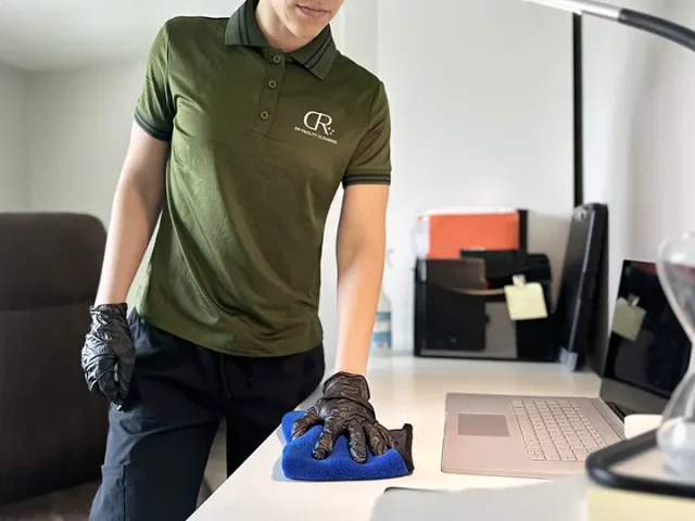 office cleaning Workplaces Professional cleaner wearing gloves wiping an office desk with a microfiber cloth in a modern workplace.